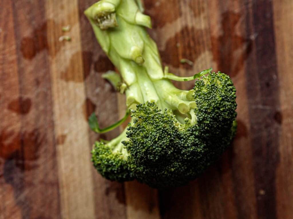 Fresh broccoli on a wooden cutting board, showing its stalk and florets in vivid green hues.